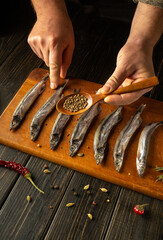 Skilled hands delicately arrange fresh fish on a wooden board, expertly adding spices from a small...