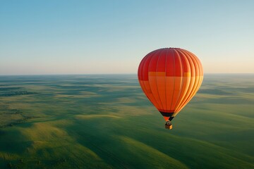 Obraz premium Orange hot air balloon floating over rolling green hills during sunrise. Aerial landscape view of summer adventure. Peaceful morning scenery for travel, tourism and outdoor activities promotion