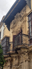 Fototapeta premium Historical building facade with ornate baroque details, iron balconies, and decorative columns; worn plaster and wooden shutters complement the architectural style;