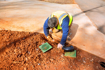 Construction worker kneels on ground, carefully installing drainage system in residential area