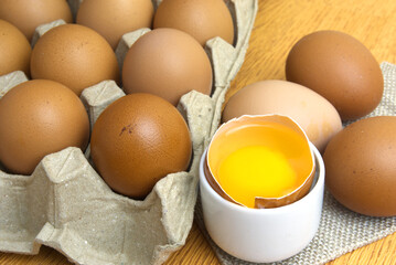 Brown-shelled organic chicken eggs One egg cracked to reveal the yolk and white with a brown shell on the side. and some eggs lay on the table