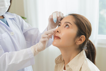 Health care concept, eye doctor eye drops to asian young woman patient, hand using medical eye drop...