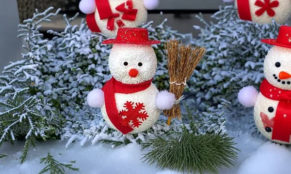 zoom sur bonhommes de neige d&eacute;coratifs avec &eacute;charpes rouges et chapeaux assortis, sur un lit de branches enneig&eacute;es, ambiance festive hivernale pour les c&eacute;l&eacute;brations de No&euml;l.