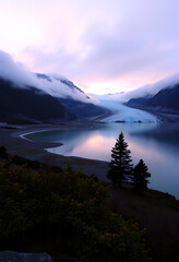 Fototapeta premium A scenic landscape of a glacier lake surrounded by mountains at twilight with soft, cloudy sky, creating a peaceful and tranquil scene.