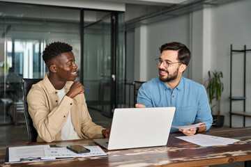 Two happy busy business men working on computers discussing online project at work. Diverse...
