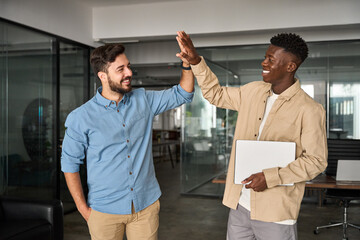 Two diverse happy professional young men teammates giving high five celebrating business triumph,...