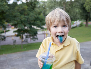 7-year-old blond boy drinks bubble tea from straw and shows his blue tongue. The concept of food coloring in children's sweets, artificial food additives, allergies to food coloring. Unhealthy sweets