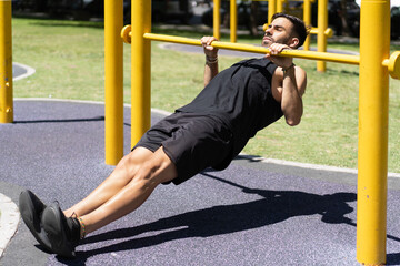 Fit young man executing inverted rows on outdoor gym bars