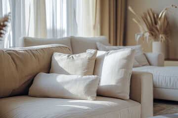 Obraz premium Cozy beige sofa with soft pillows in a bright living room filled with natural light and neutral decor.