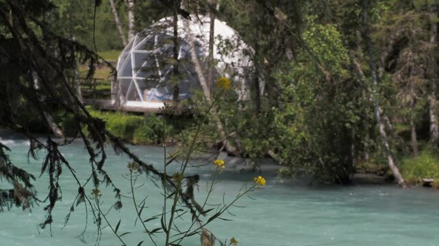 Seasons, summer. A transparent igloo built for recreation is located on the banks of a stormy mountain river among the trees. Hand held. Siberia.