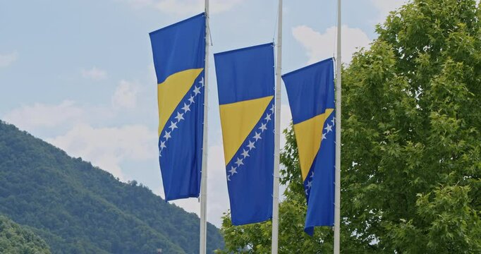 Flags of Bosnia and Herzegovina at half-mast in front of the Srebrenica Memorial Center, with nature in the background. Concept of remembrance, mourning, and honoring genocide victims