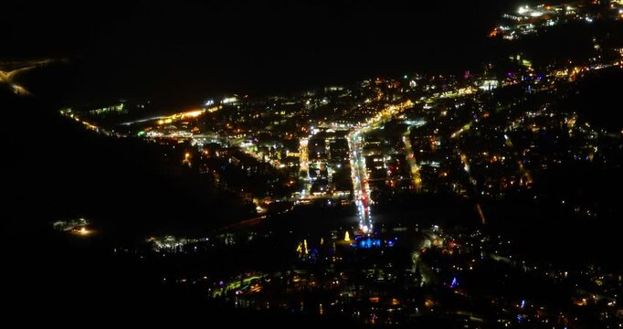 Aerial night view of the Town of Banff nestled in a valley with twinkling lights and roads illuminating the landscape in Alberta, Canada. 