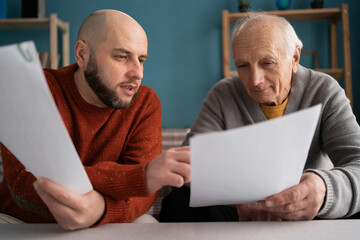 Caucasian millennial man helping parent and explaining some documentation or bill papers to senior...