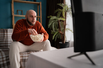 Concept of weekend leisure activities. Millennial man watching TV at home and eating popcorn while watch interesting program on television