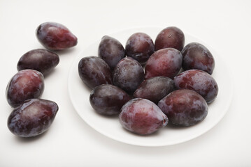 Fototapeta premium Fresh black plums on a white plate. Freshly washed plums. Juicy fruits.