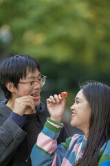 Obraz premium Young Chinese couple in their 20s eating Beijing's famous sugar-coated fruit sweets on a sidewalk in Hongkou District, Shanghai, People's Republic of China, in the evening, December 2024.