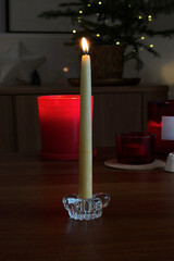 Burning candle in a glass candleholder in a cozy festive decorated living room.