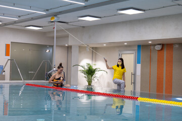 A hydrotherapy session in a modern rehabilitation center. A therapist monitors a patient using a secure harness system in a pool designed for aquatic therapy and recovery.