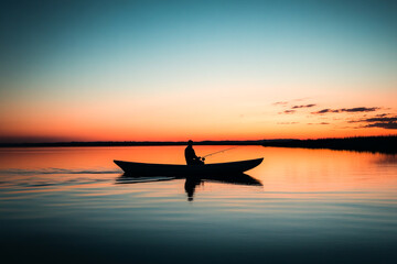 Obraz premium Silhouette of a person fishing in a canoe on a serene lake at sunset