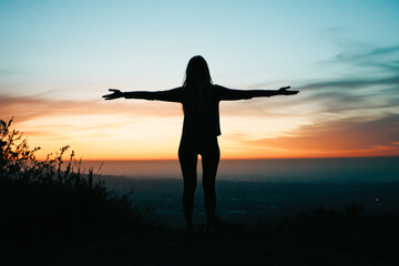 Fototapeta premium Silhouette of young female embracing sunset with open arms