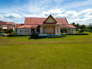 Obraz premium Laos Style Building: A traditional Lao-style building with a red tiled roof and an open-air stage stands proudly on a manicured lawn under a bright blue sky.