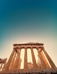 Fototapeta premium Ancient Greek temple ruins bathed in warm sunlight against a vibrant blue sky.