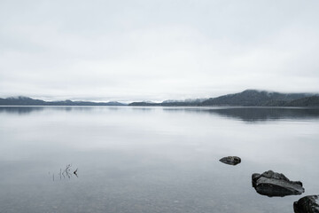 Naklejka premium Moody lake on Vancouver Island, Canada, with mountains in the background on a cloudy november day