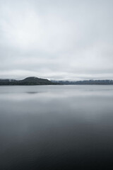 Obraz premium Moody lake on Vancouver Island, Canada, with mountains in the background on a cloudy november day