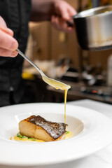 A chef elegantly drizzles rich sauce over a beautifully plated piece of fish, showcasing culinary...