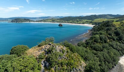 Naklejka premium Panoramic view of a pristine beach nestled amongst lush New Zealand foliage. Coastal scenery with a tranquil bay. NEW CHUMS BEACH, WHANGAPOUA, COROMANDEL PENINSULA, NEW ZEALAND