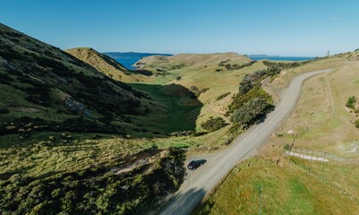 Naklejka premium Aerial view of a rural road winding through a grassy valley, with a parked car. Scenic countryside landscape. , OTAMA, COROMANDEL PENINSULA, NEW ZEALAND