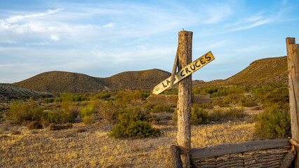 Wooden Signpost in Desert Landscape: Rustic La Cruces Directional Marker Amidst Barren Hills and Arid Vegetation, Showcasing Natural Wilderness and Serenity