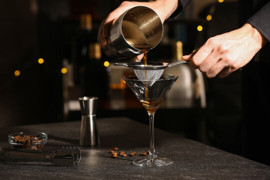 Bartender making delicious espresso martini at dark table against blurred lights, closeup