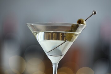 Martini cocktail with olives in glass on blurred background, closeup. Bokeh effect