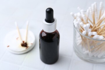 Bottle of iodine with dropper, cotton pads and swabs on white tiled table, closeup