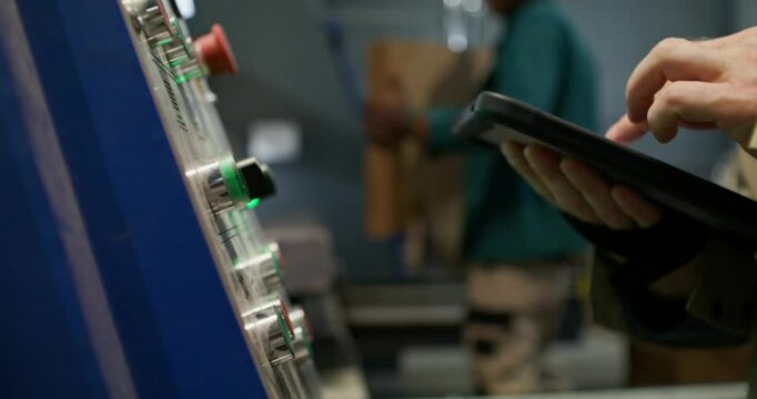 Work in a paper mill. A man uses a tablet to control the operation of the machine