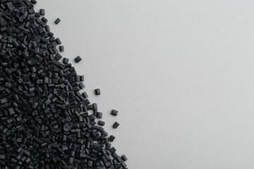 Pile of black plastic granules on grey background, top view. Space for text