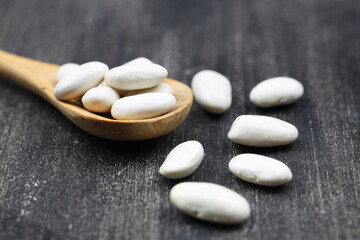 White Beans in a wooden spoon close-up on a wooden background. Vegetarian food.