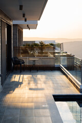Stylish balcony with a table and chairs, illuminated by sunset light, overlooking a serene...