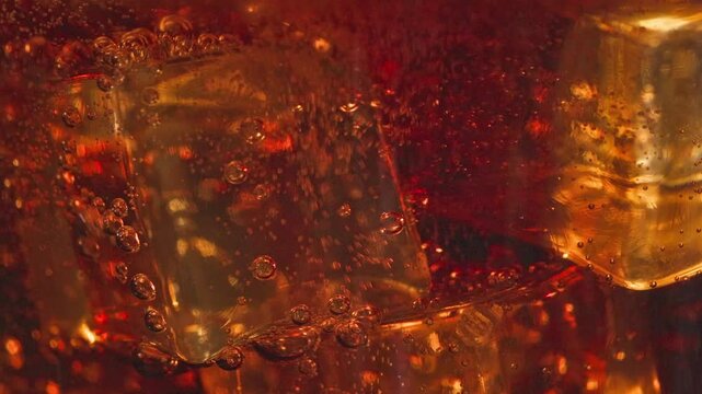 fresh cola pouring into glass with ice, close up. bubbles move around ice cubes macro