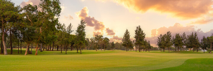 A tranquil golf course framed by lush greenery and bathed in the warm glow of a colorful sunset sky.
