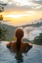 Fototapeta premium Woman relaxes in infinity pool overlooking foggy mountain sunrise. Luxury tropical travel