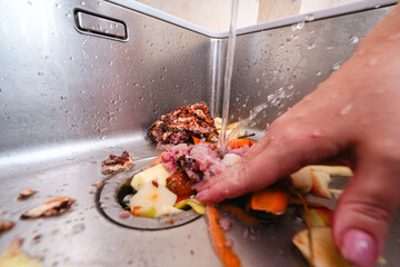 Removing food scraps with running water and garbage disposer in a kitchen sink.