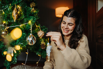 Young caucasian woman putting Christmas decoration on Christmas tree