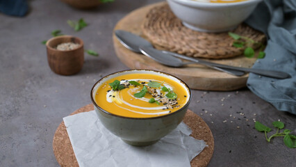 A creamy pumpkin soup garnished with sesame seeds and a swirl of yogurt, served in a bowl on a rustic table