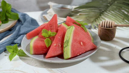 Watermelon slices arranged on a plate, garnished with mint leaves and a honey dipper nearby