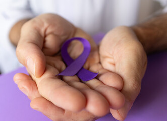 Crossed hands of man holding purple ribbons.World cancer day concept.