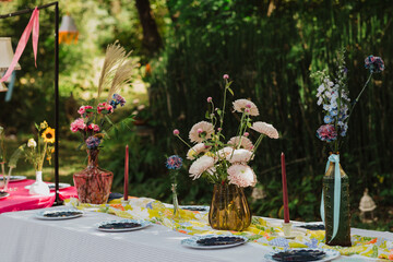 Garden Party Table Decor with Amber and Glass Vases, Pink Chrysanthemums, Colorful Floral Runner, and Elegant Plates in a Serene Outdoor Setting