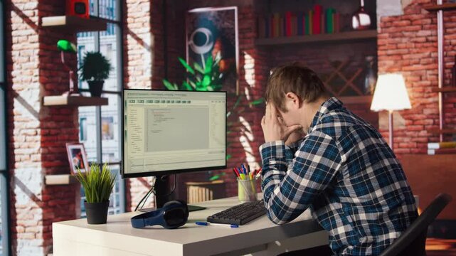 Coder at workstation programming on PC, writing lines of code, using development tools, feeling stressed. Man in home office having deadline, stressed to finish debugging software, camera A