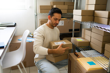 Good looking man manages a small business from a storage room, diligently preparing packages for...